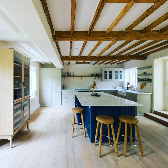 Light wood plank flooring through an open kitchen and living area with exposed beams