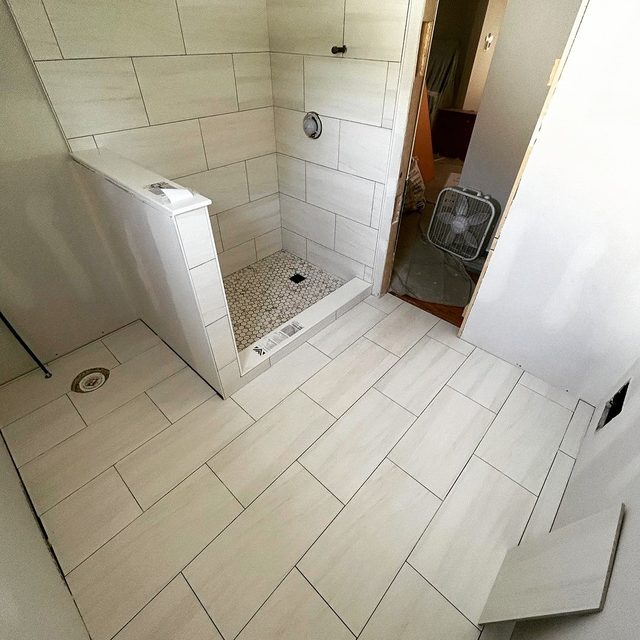 Tiled shower with half wall and a large-format tile bathroom floor laid on a diagonal