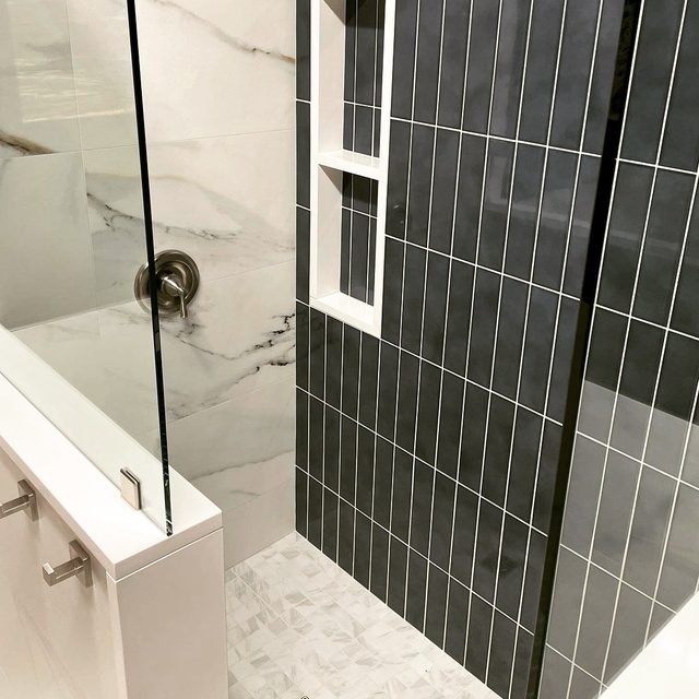 Detail of a recessed shower niche in charcoal vertical tile beside marble-look porcelain